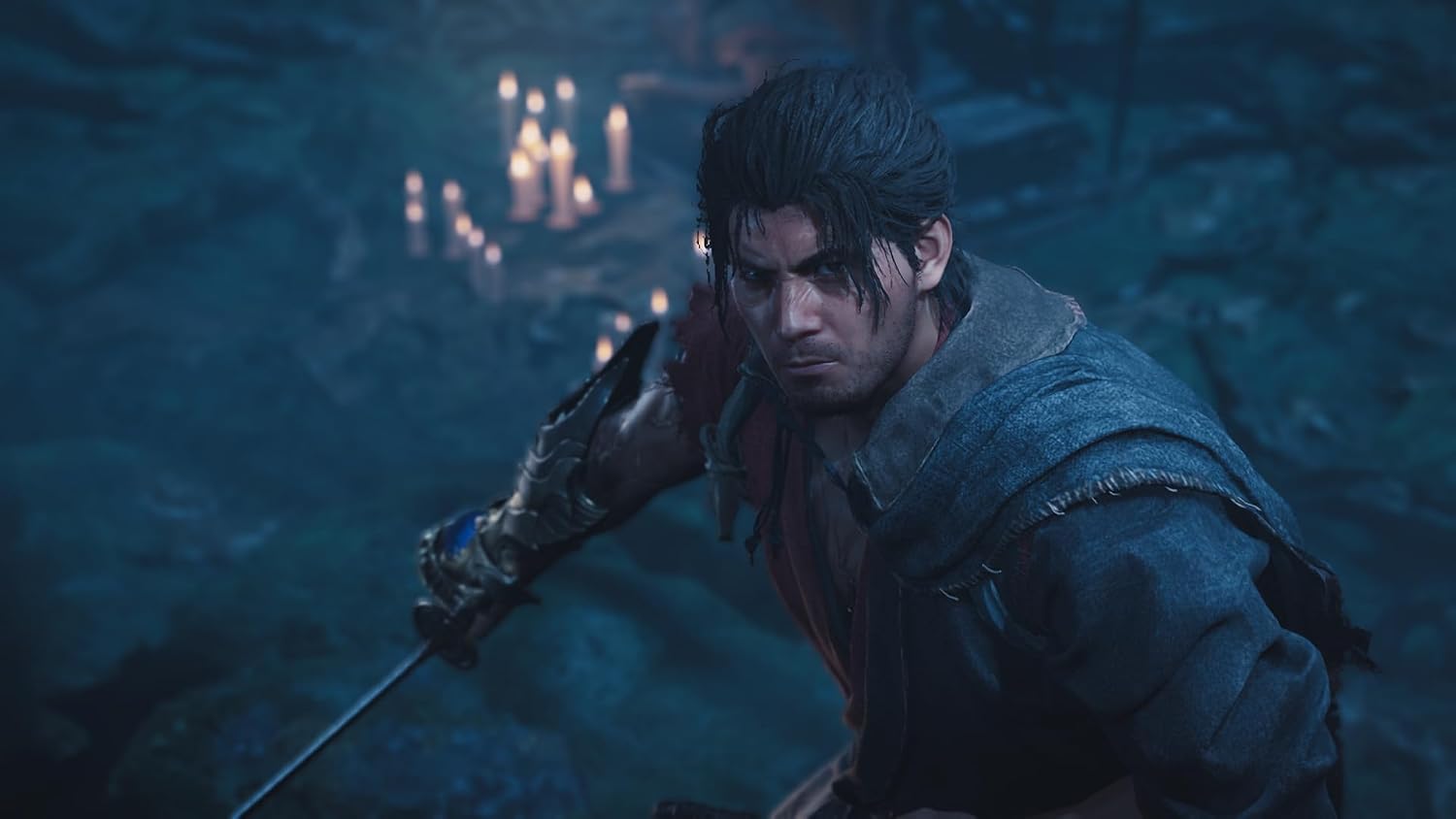 A video game character in a dark blue cloak and brown tunic, holding a sword in a dimly lit blue stone environment with candles in the background.
