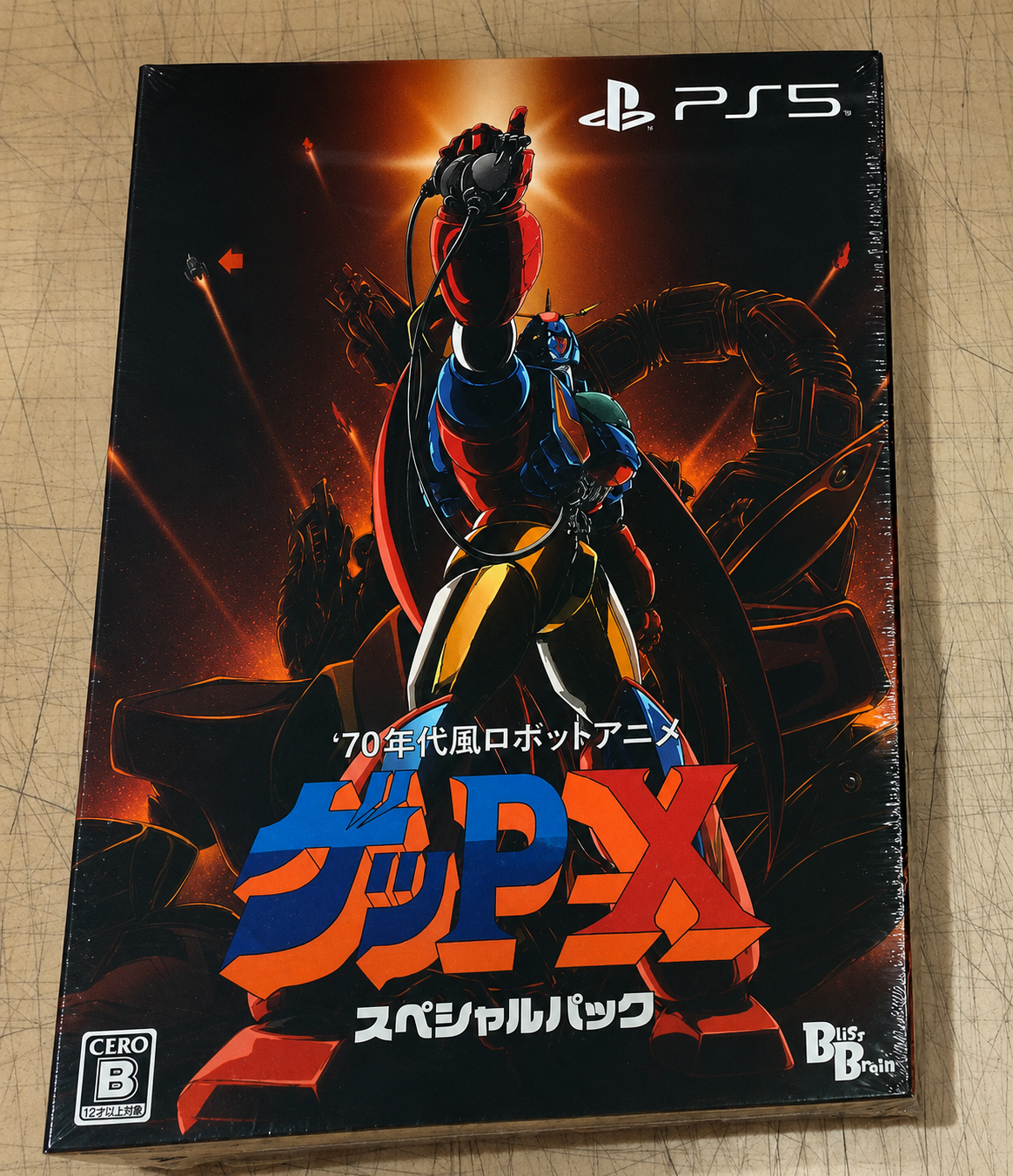 PS5 game case for GUP-X Special Pack, featuring a dynamic robot illustration in red, blue, and yellow against a fiery orange and black background, photographed on a light wood surface.