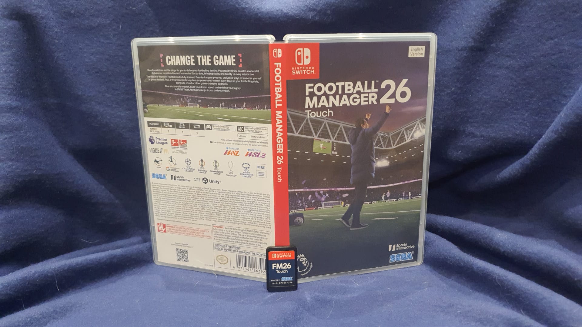 Football Manager 26 game case and microSD card on a blue fabric background