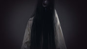 Person wearing a long black hooded garment against a dark background
