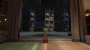 A small orange tabby cat sits on a tiled floor in a dimly lit room, looking out toward a large warehouse or storage area with tall blue shelving and stacked boxes.