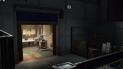 A dimly lit warehouse or industrial interior with a large open overhead door revealing a warmly lit office or room inside. To the right is a fenced storage area with stacked boxes and pallets.