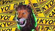 A lion costume headpiece or lion mask with a brown mane, white muzzle, and green glowing accents, set against a background of yellow caution tape printed with 'TOKYO!' and Japanese characters.