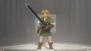 A collectible action figure of Link from The Legend of Zelda, standing on a light-colored platform in a misty gray environment. The figure is wearing his signature green tunic, white trousers, and brown boots, and holds a large sword over his shoulder.