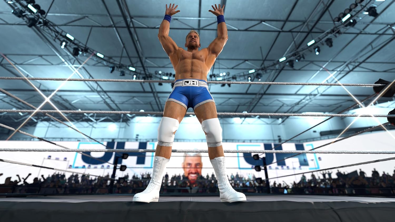 Wrestler in blue trunks standing in a wrestling ring with a crowd in the background